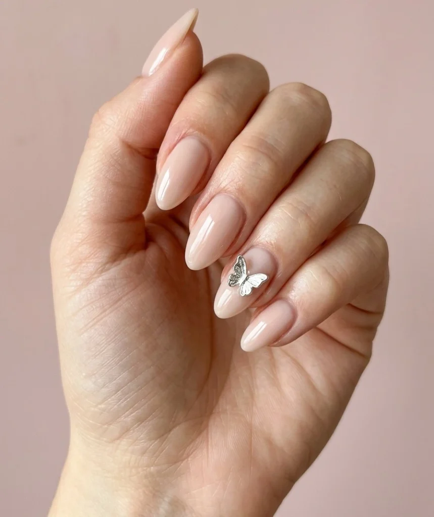 Cool girl nail designs in milky nude with a single silver chrome butterfly accent nail on almond nails