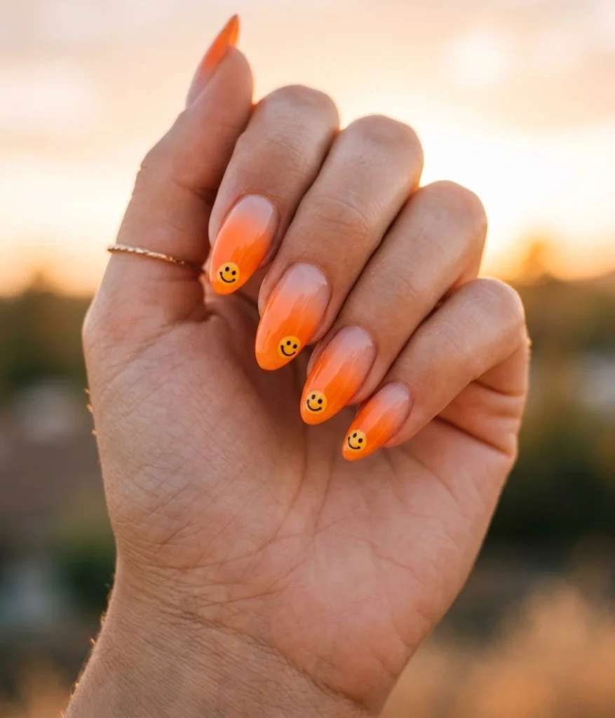 Summer smiley face nails with orange ombre tips and a glowing sunset smiley face on medium almond nails