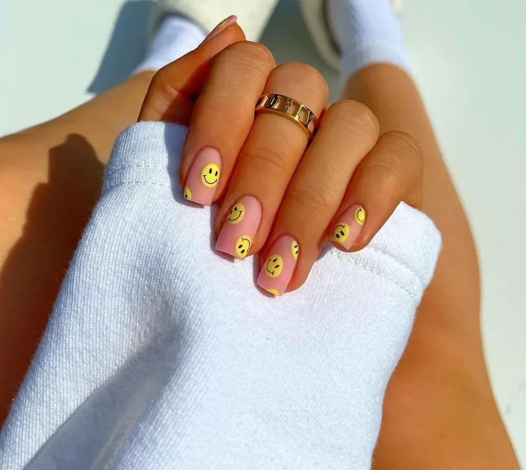 Summer smiley face nails with sheer pink base and scattered yellow smiley accents on short squoval nails