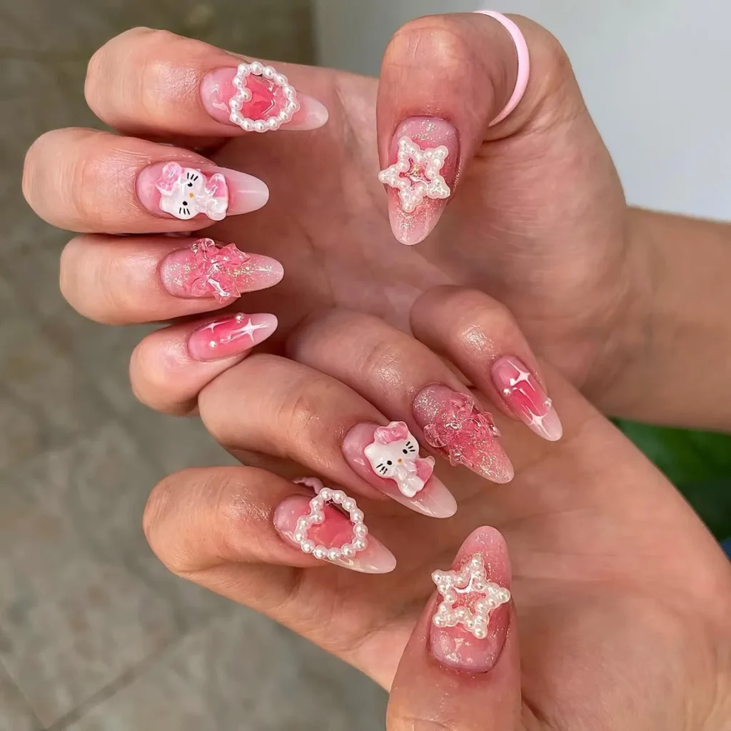 Pink Hello Kitty nails with 3D pearl hearts, pearl stars, glitter, and a raised Hello Kitty accent on almond nails