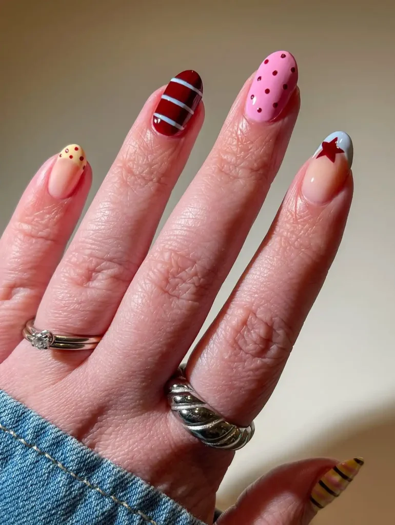 Mismatched cool girl nail designs with burgundy stripes, red dots, and a tiny star on short almond nails