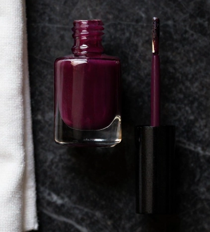 dark plum nail polish bottle and cleanup brush flat lay on marble