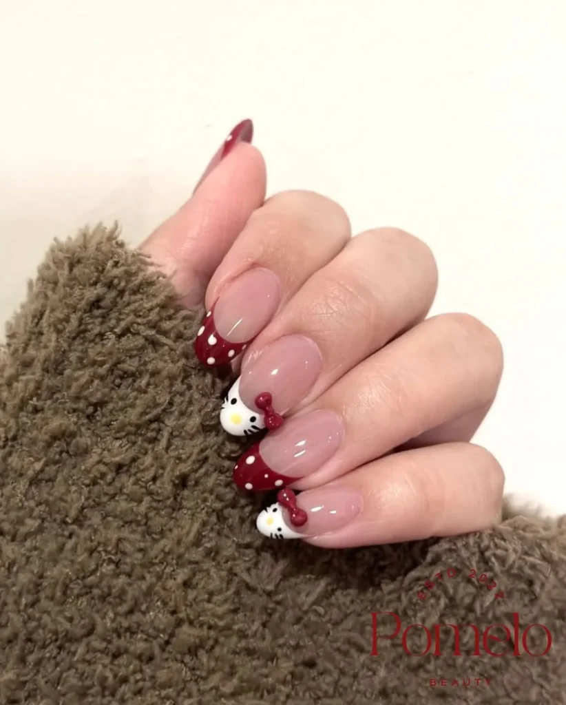 Deep burgundy French Hello Kitty nails with white polka dots, white Kitty face tips, and raised 3D red bows on medium almond nails