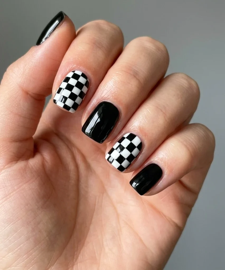 Cool girl nail designs in a crisp black and white checkerboard with solid accent nails on short square nails