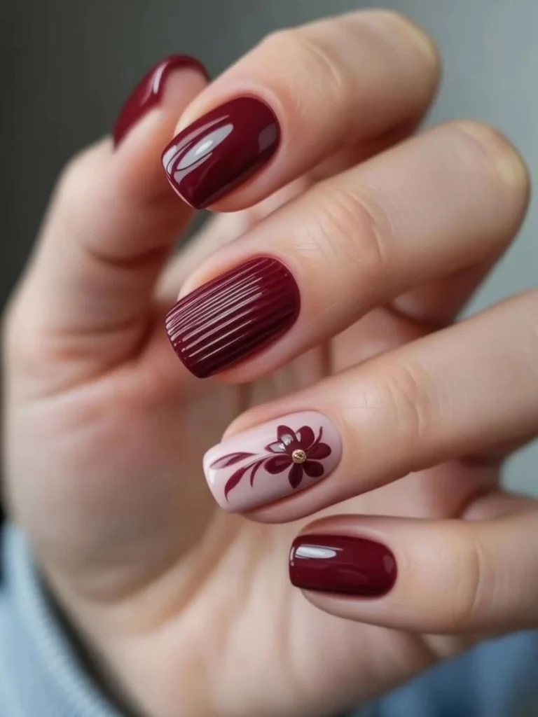 Cool girl nail designs in glossy deep burgundy with a ribbed textured nail and a pink floral accent with a gold stud on short square nails