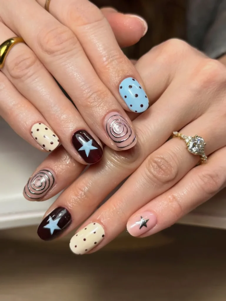 Cool girl nail designs with hand drawn swirl doodles, dots, and stars in moody burgundy, cream, and sky blue on short round nails
