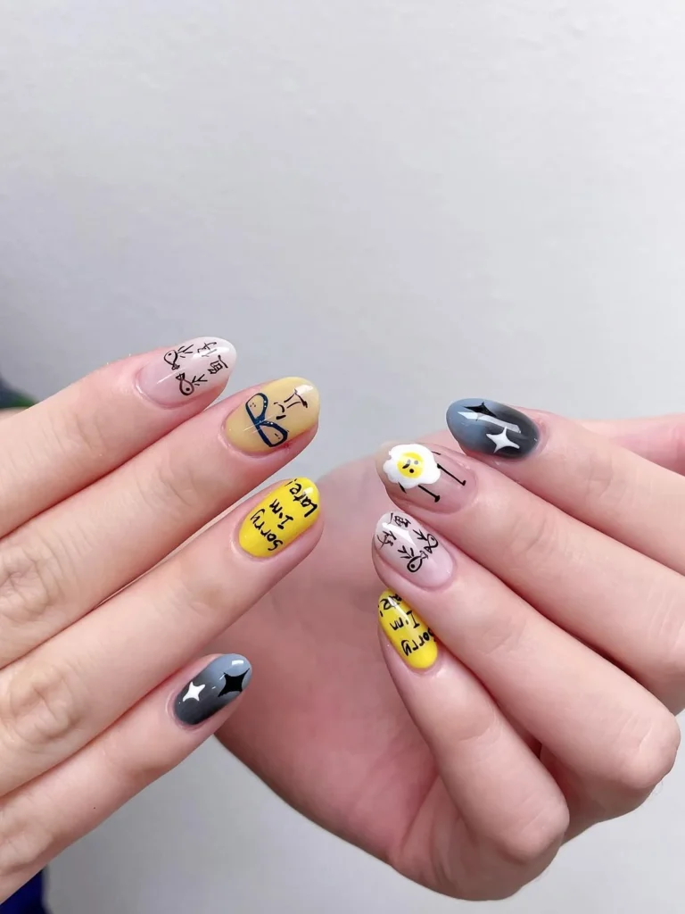 Playful cool girl nail designs with hand drawn doodles, text, a fried egg, and sparkles in yellow, grey, and nude on short round nails