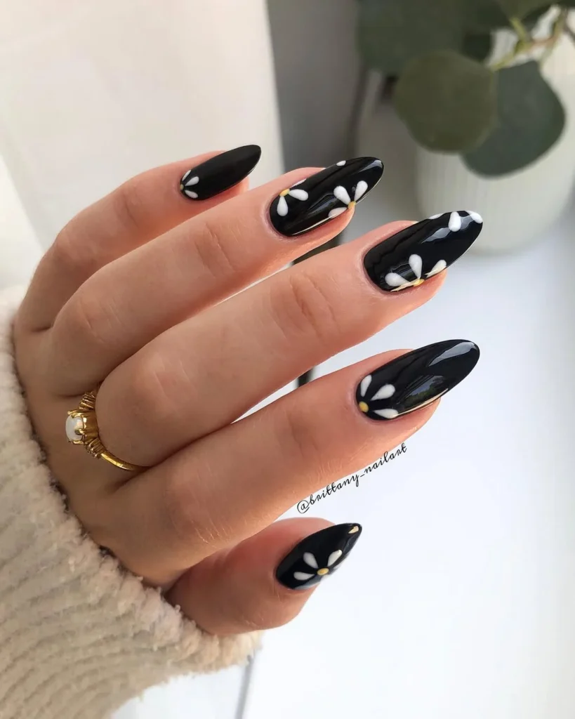 Cool girl nail designs in glossy black with off center white daisies and yellow centers on long almond nails