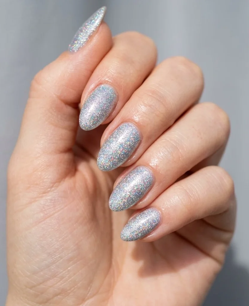 Cool girl nail designs in icy silver holographic glitter with rainbow flecks on short almond nails