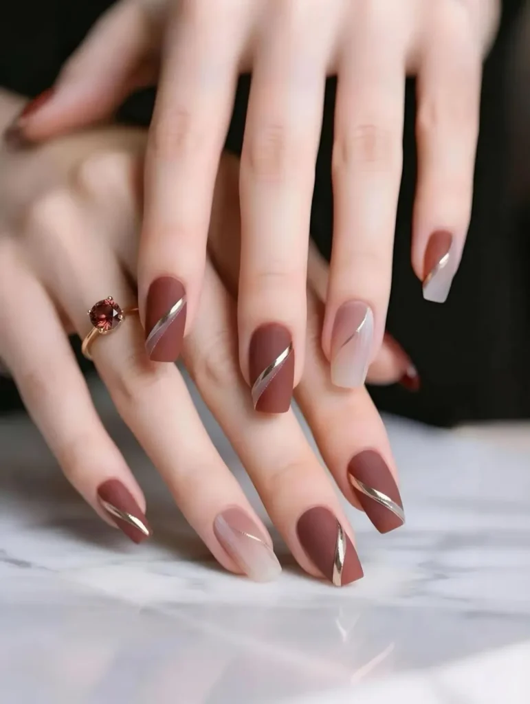 Matte terracotta cool girl nail designs with thin gold diagonal lines and nude accent nails on long square nails
