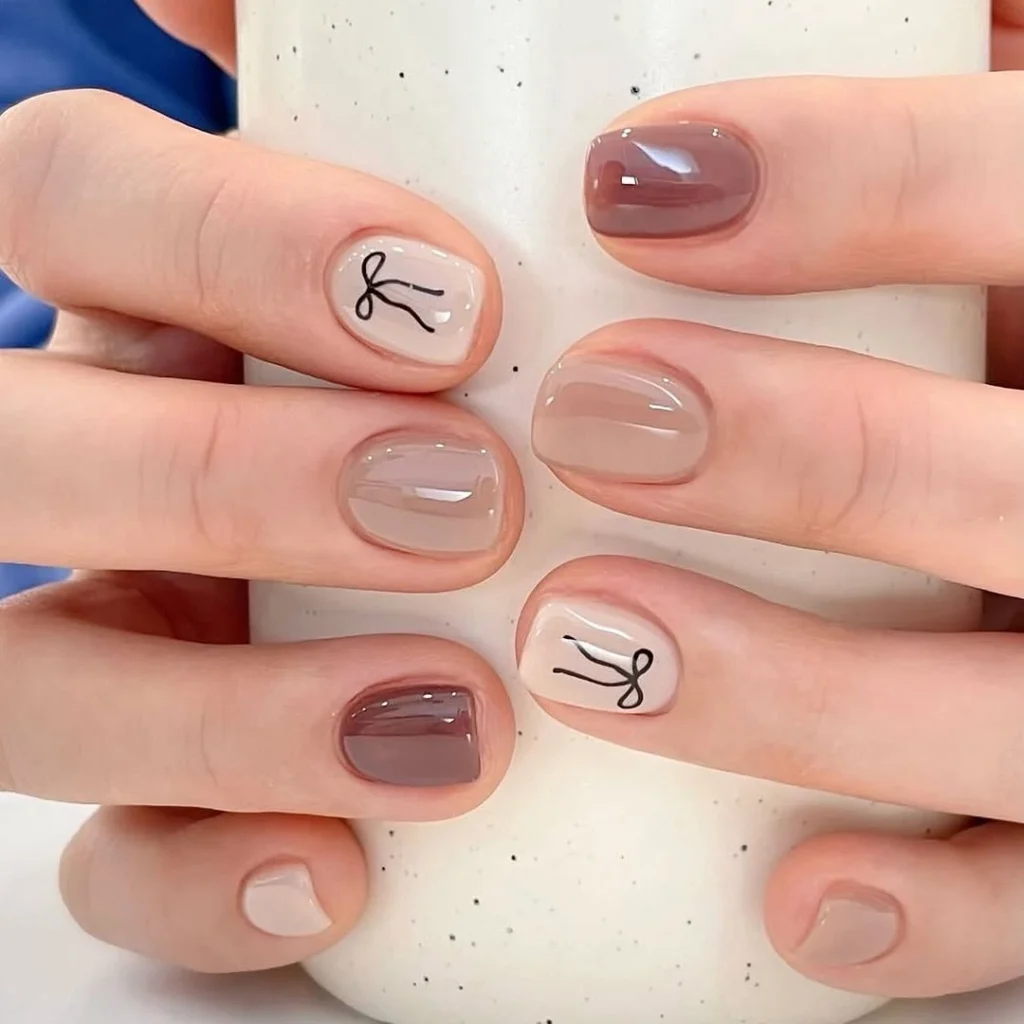 Short neutral cool girl nail designs in milky brown shades with tiny black line bow art on square nails