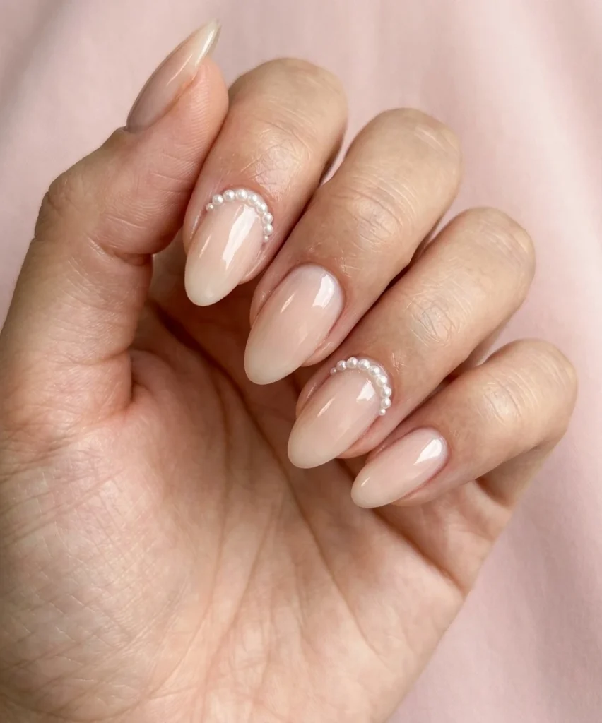 Cool girl nail designs with a sheer nude base and tiny pearl cuff detail at the cuticle on almond nails
