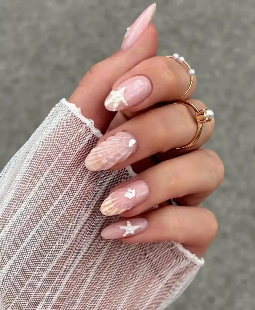 Cool girl nail designs in sheer pearly nude with 3D white starfish and seashell details on long almond nails