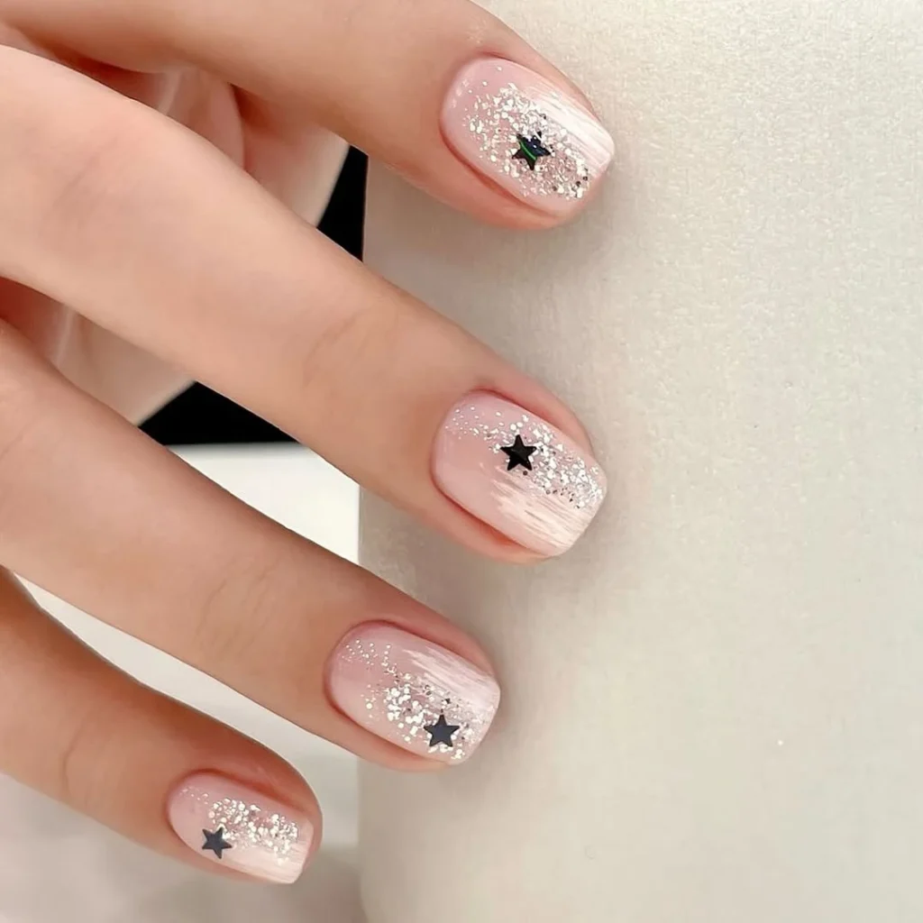 Sheer nude cool girl nail designs with faded silver glitter and tiny black stars on short square nails