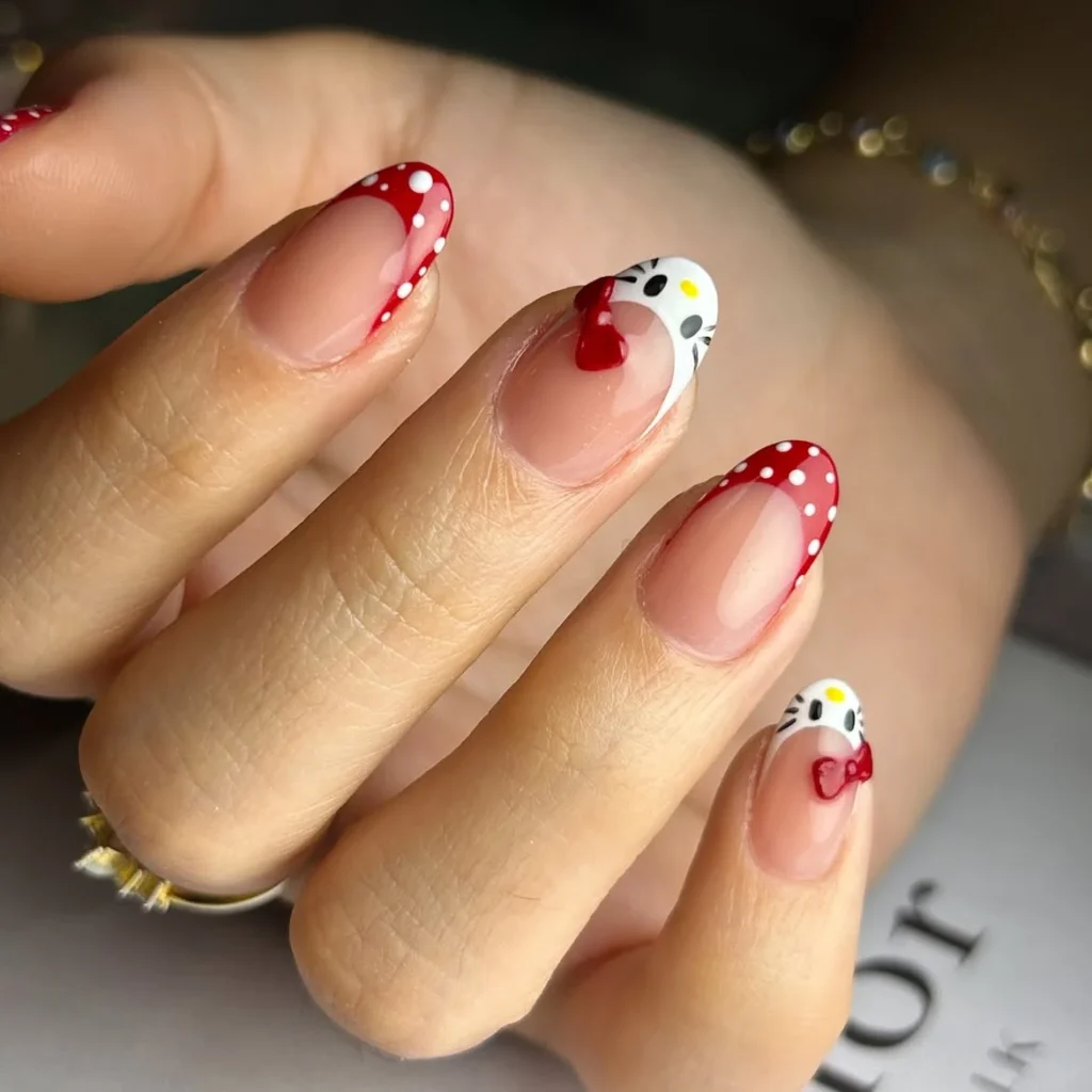 Retro red French Hello Kitty nails with white polka dots, Kitty face tips, a red bow, and a 3D heart on short almond nails