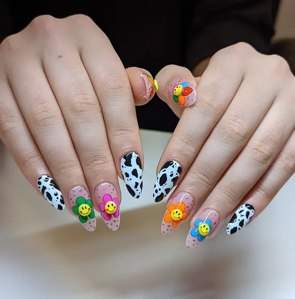 Summer smiley face nails with 3D smiley flower charms and black and white cow print on long almond nails
