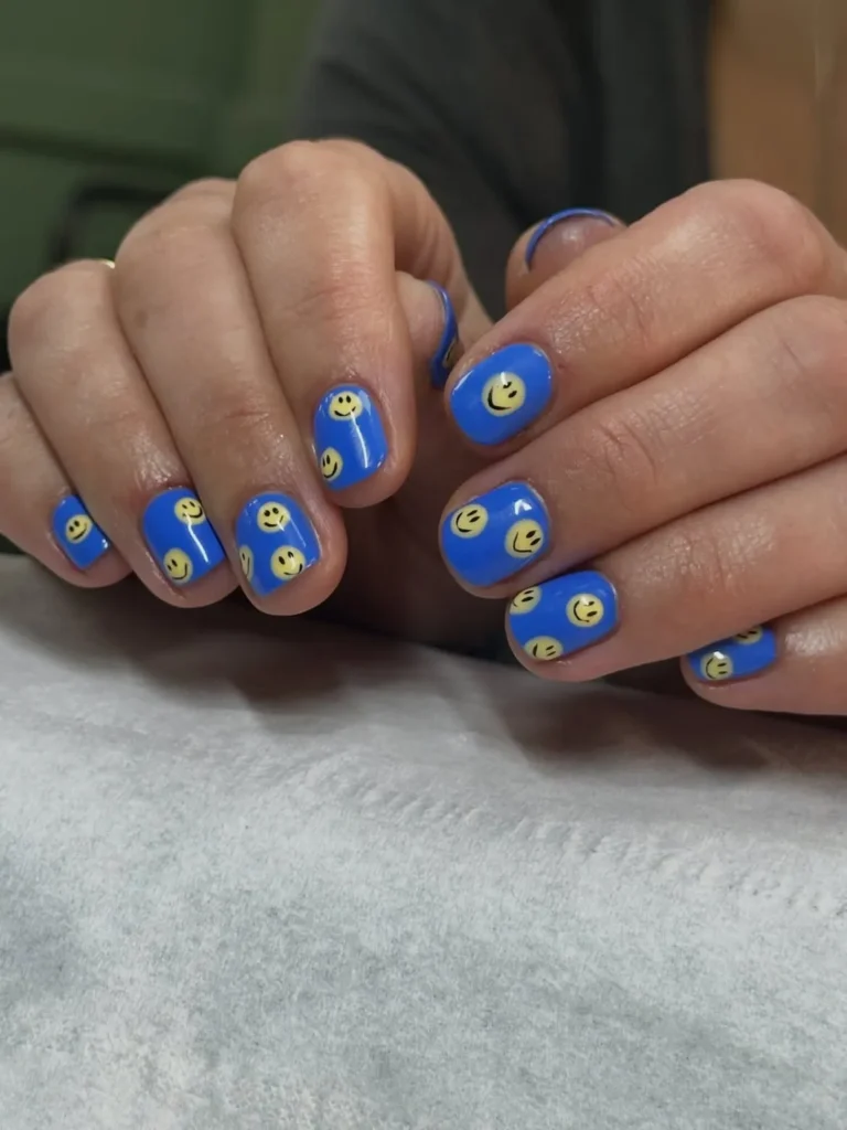 Summer smiley face nails with bold cobalt blue base and yellow smiley faces on short square nails