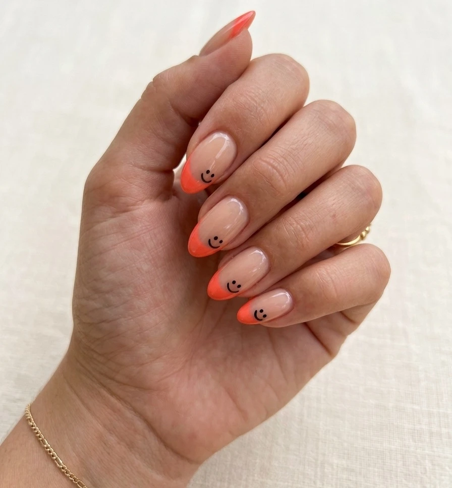 Summer smiley face nails with coral French tips and tiny corner smiley faces on medium almond nails