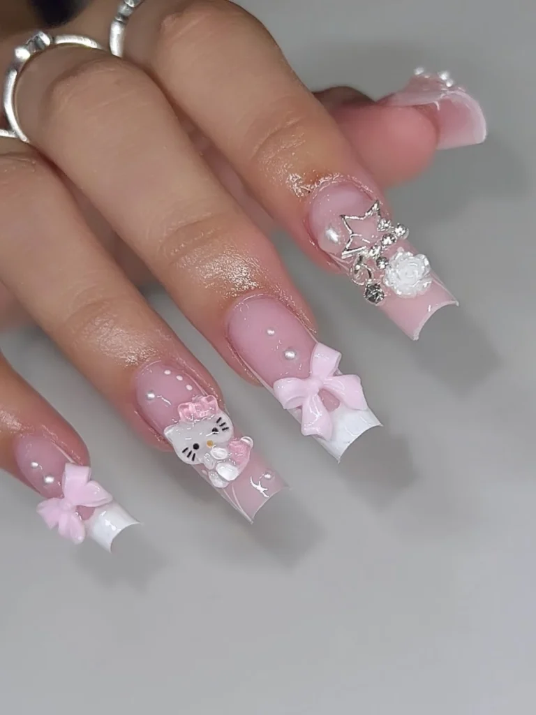 Long square white French Hello Kitty nails with a 3D Kitty charm, pink 3D bows, pearls, and a silver star and rose accent on a pale pink base